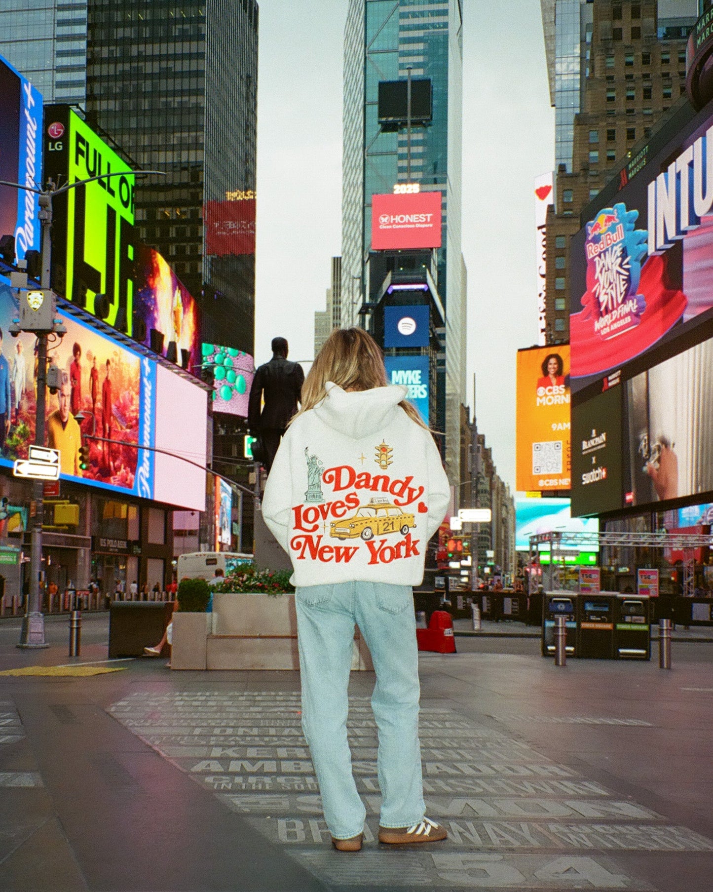Person wearing a sweatshirt with 'Dandy Loves New York' text in Times Square, New York.