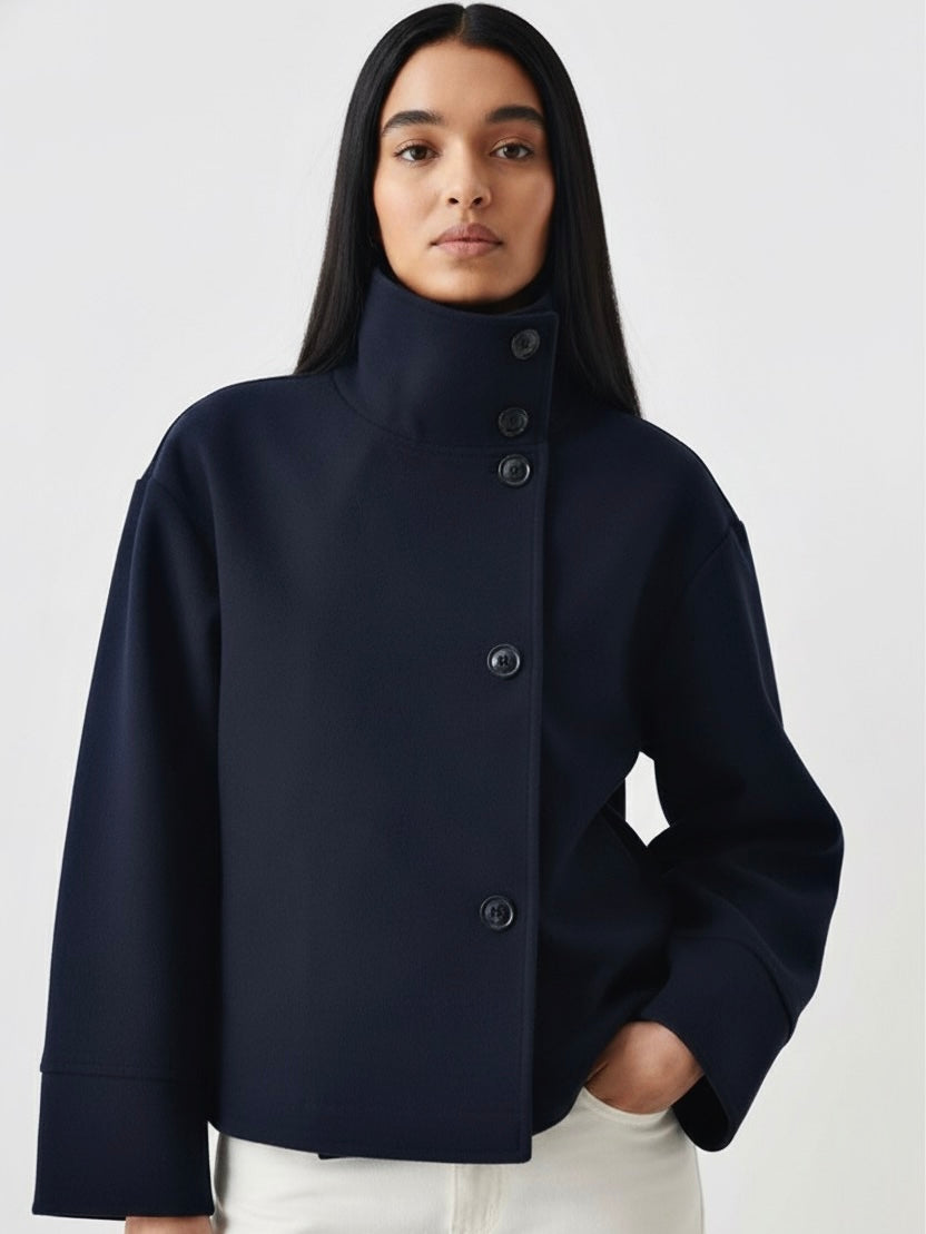 Black high-neck jacket with asymmetrical buttons and structured silhouette, featuring wide sleeves and a minimalist design for modern everyday styling.